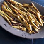 Roasted parsnips being served on a brown ceramic platter.