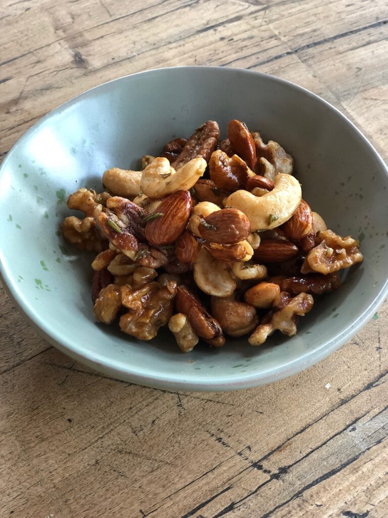 Roasted nuts made with maple syrup and rosemary in a small snack bowl.