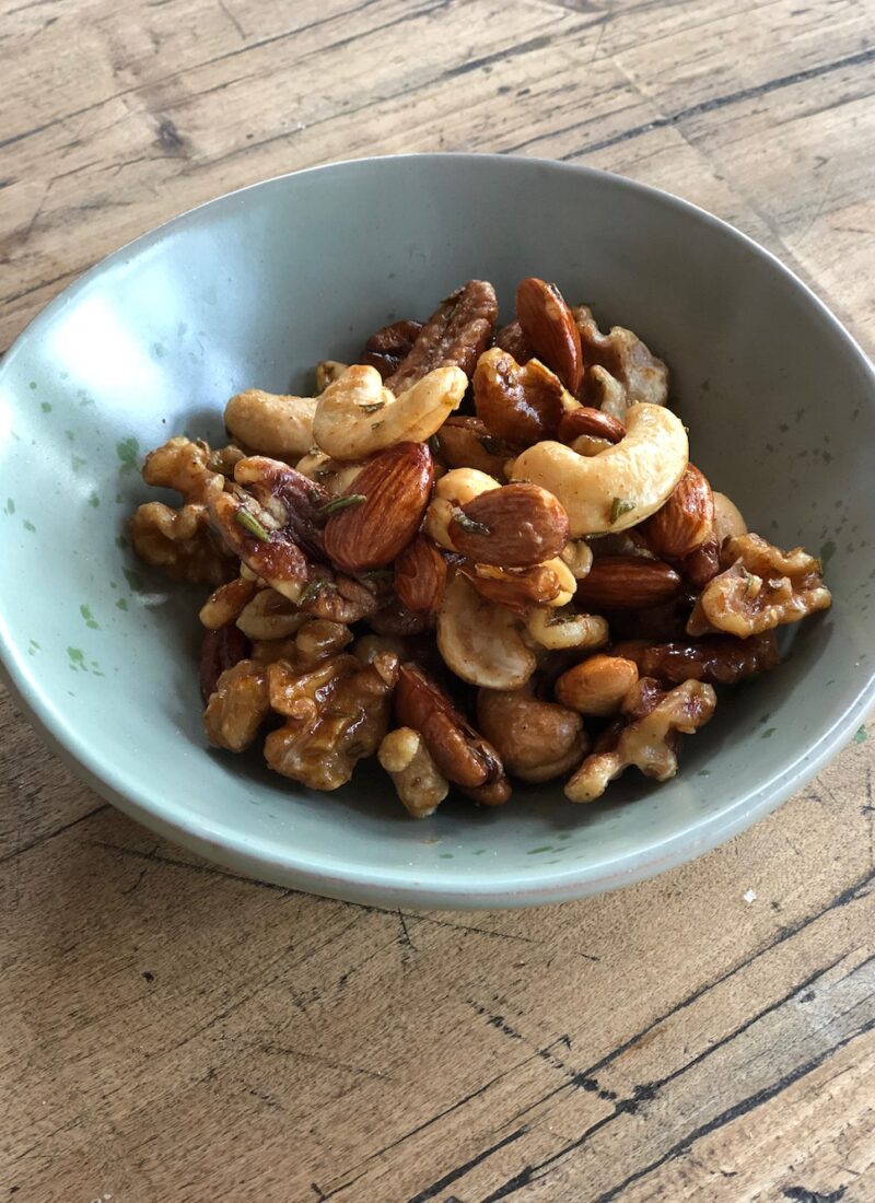 Roasted nuts made with maple syrup and rosemary in a small snack bowl.