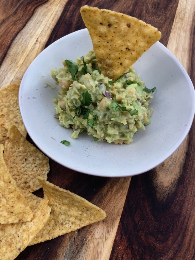 Small bowl of chickpea guacamole with some tortilla chips.