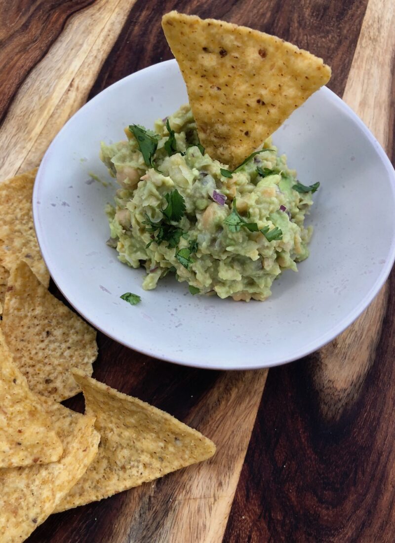 Small bowl of chickpea guacamole with some tortilla chips.