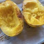 Baked spaghetti squash cut in half on a parchment-line baking pan.