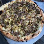 A pizza with red onion, rosemary, and pistachios toppings.