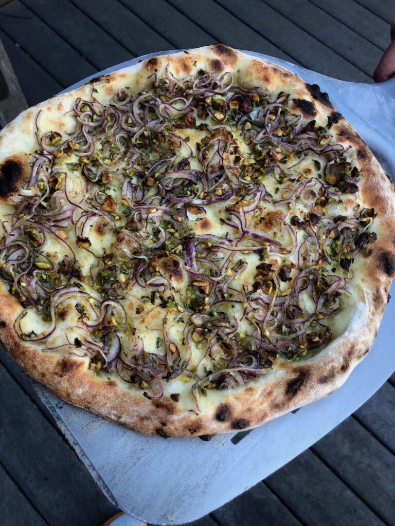 A pizza with red onion, rosemary, and pistachios toppings.