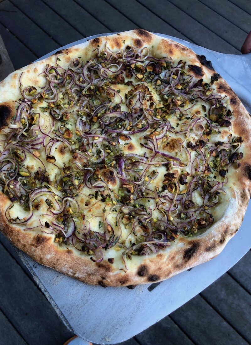 A pizza with red onion, rosemary, and pistachios toppings.